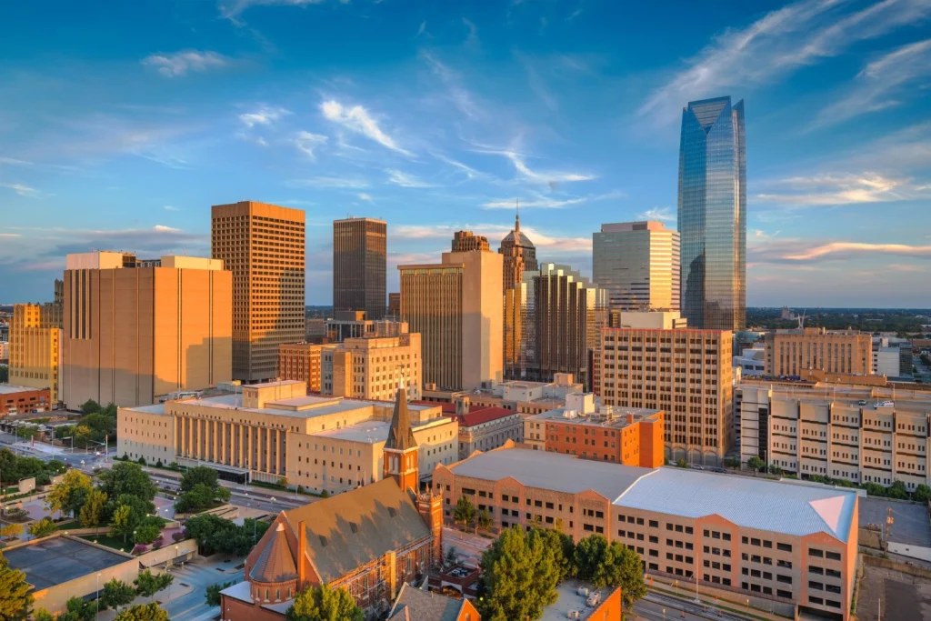 Downtown Oklahoma City, OK skyline at sunset, featuring modern high-rise buildings, historic architecture, and warm golden light illuminating the urban cityscape.